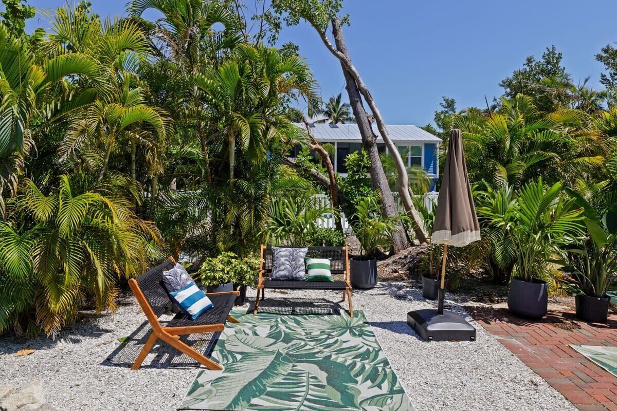 Un área de estar al aire libre tropical con un banco, sillones de descanso y un tapete estampado.