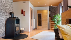 Una sala de estar moderna con una pared de piedra, una chimenea negra, suelo de madera, un sofá y una escalera que sube a un altillo.