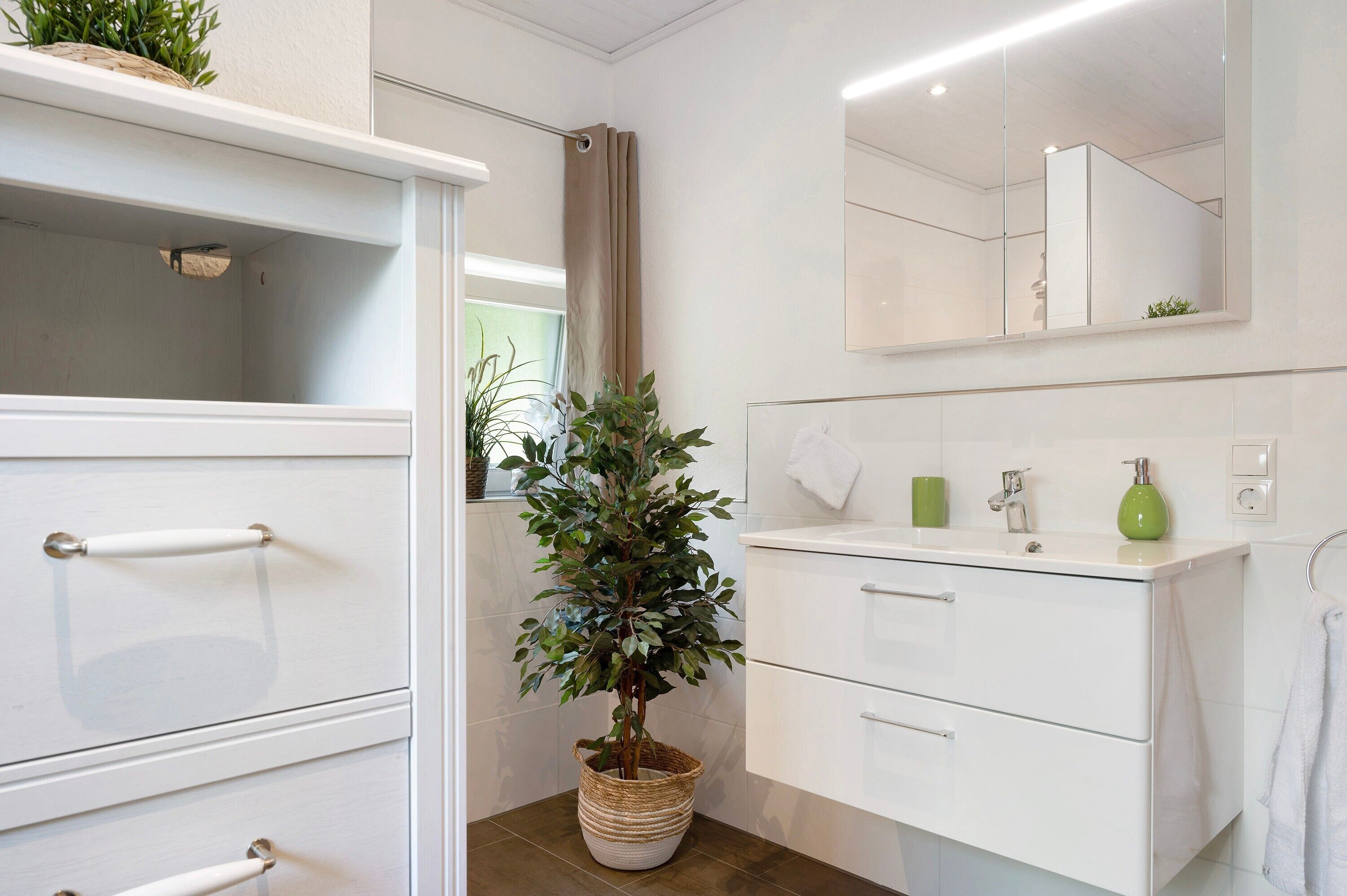 Une salle de bain moderne avec un meuble-lavabo blanc, un grand miroir et une plante en pot.
