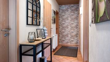 A hallway with a wooden door, a black-framed mirror, a radiator, and a brick wall.