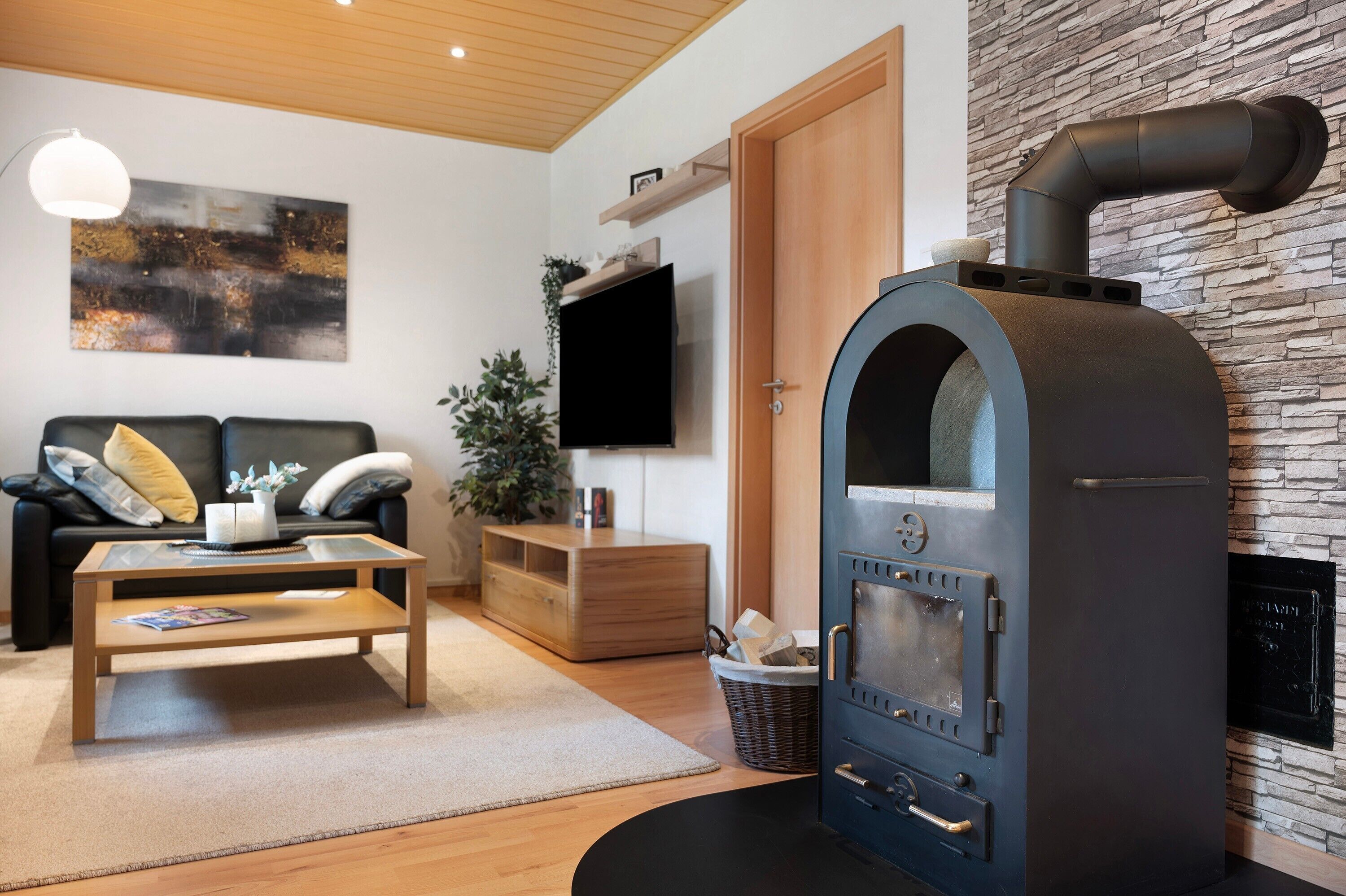 A modern living room with a stone wall, a sofa, a coffee table, a TV, and a wood-burning stove.