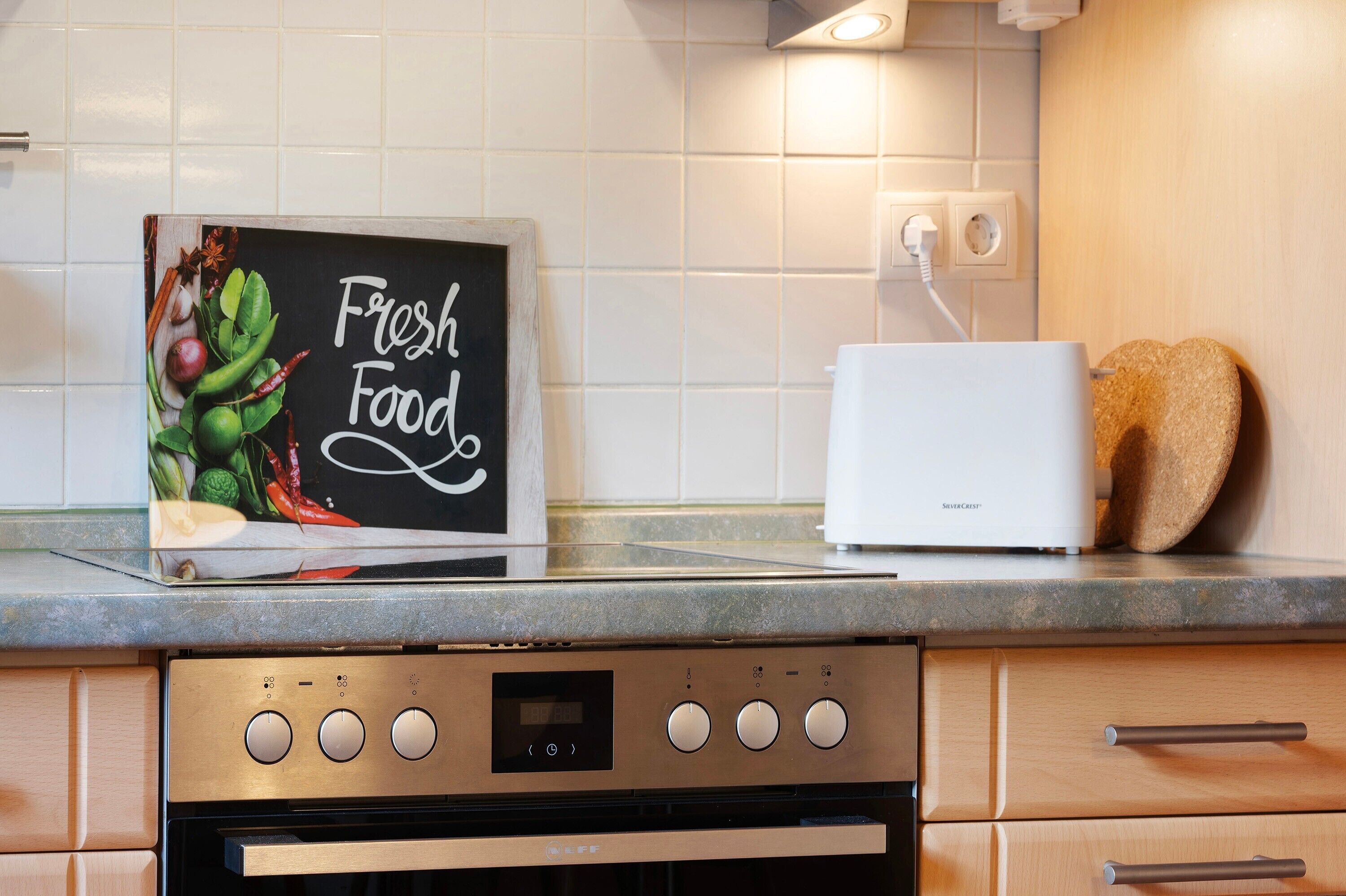 Eine Küche mit digitaler Anzeige, die 'Frische Lebensmittel' anzeigt, einem weißen Toaster und einem eingebauten Backofen.