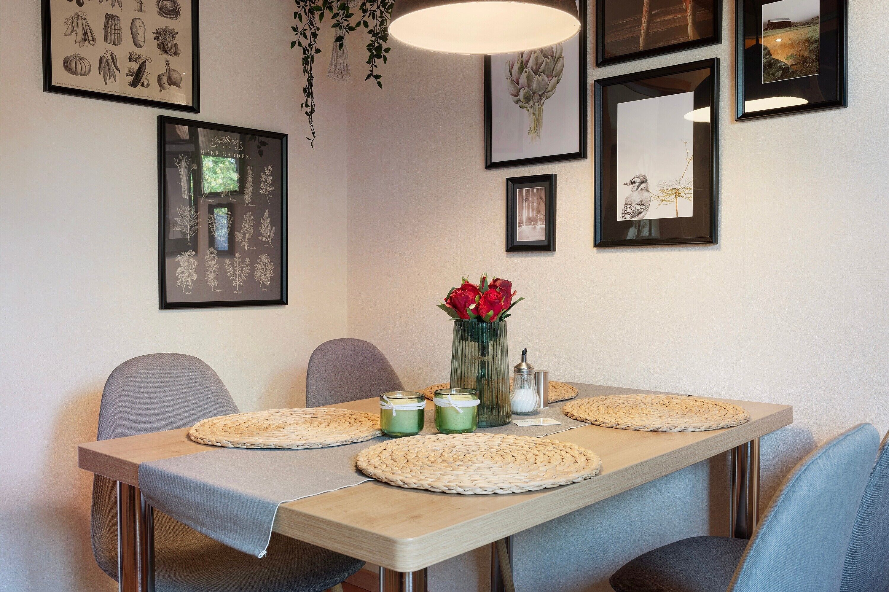 Ein Essbereich mit Tisch für vier Personen, gerahmten Pflanzenbildern an der Wand und einer Vase mit roten Blumen.