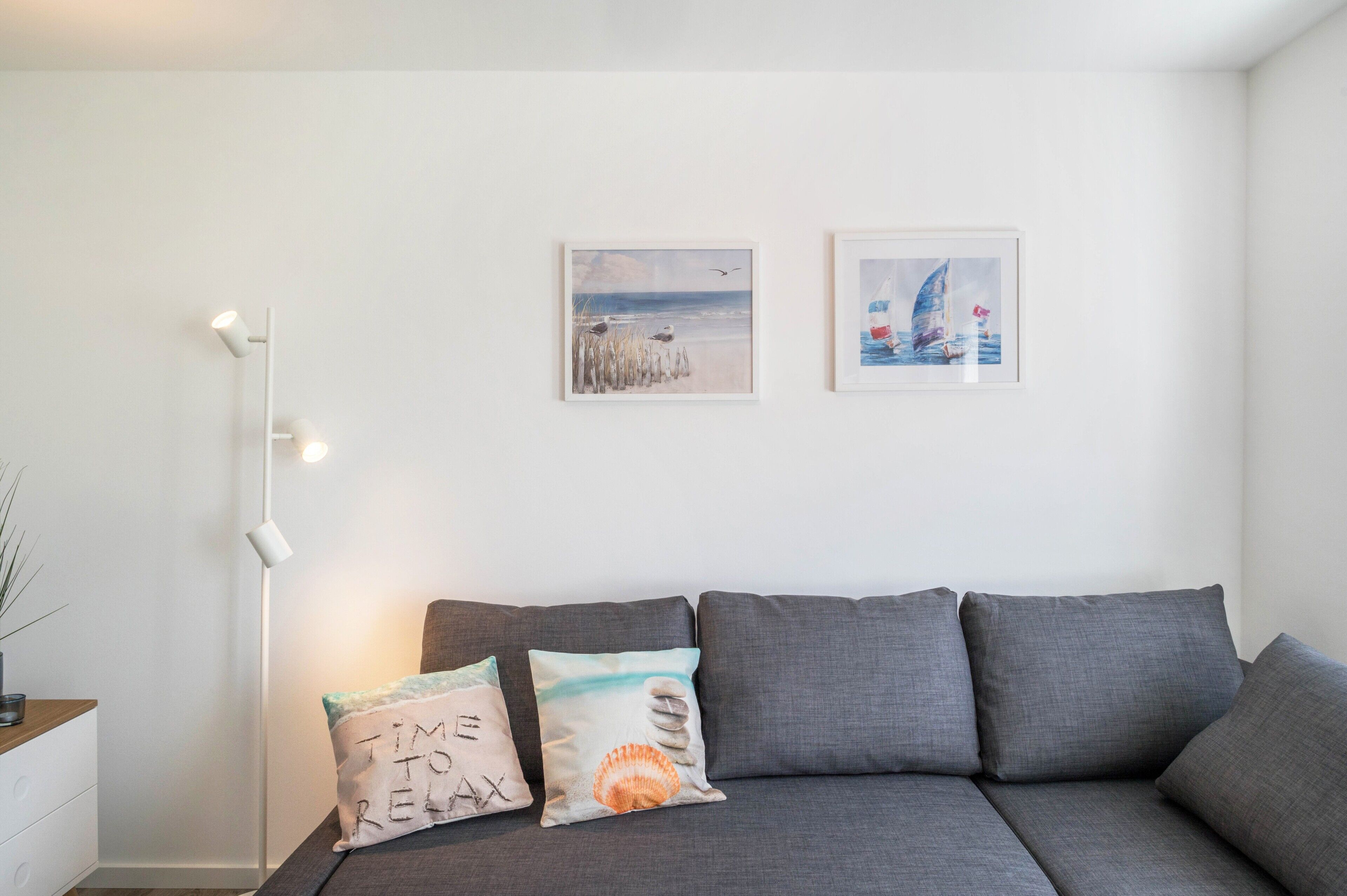 Ein modernes Wohnzimmer mit einem grauen Sofa, zwei Wandgemälden und einer Stehlampe.