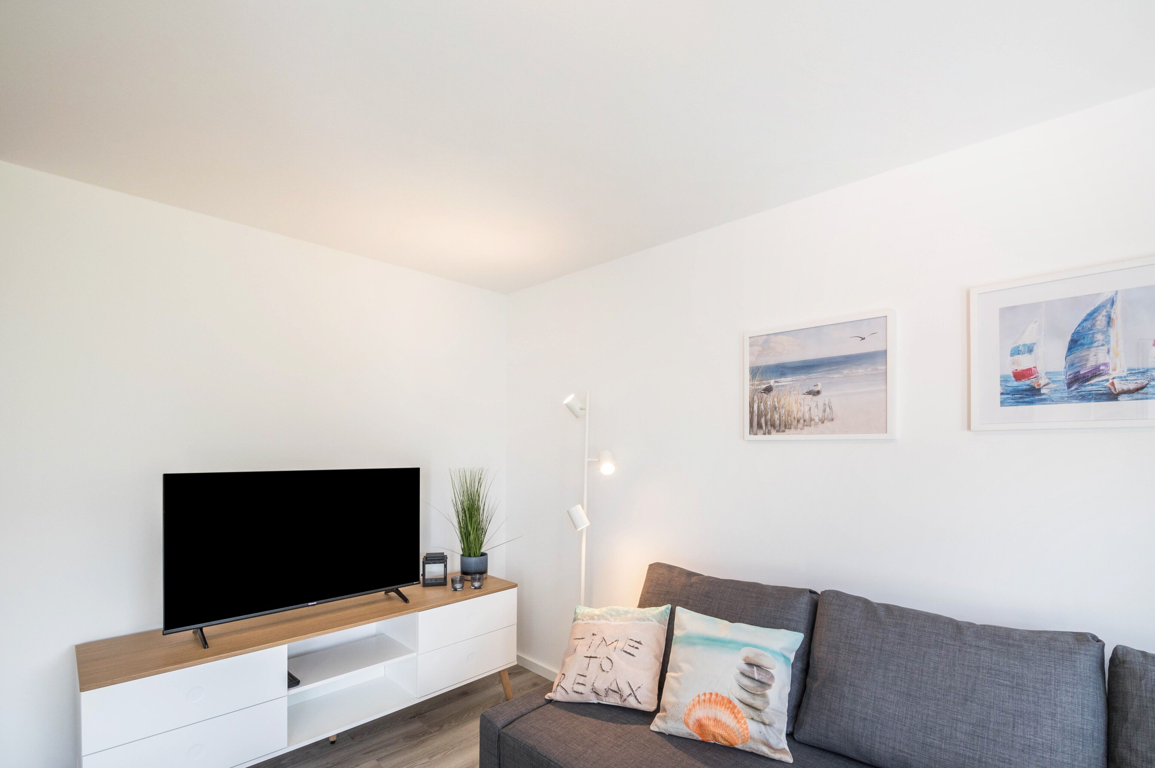 Un salon moderne doté d’un téléviseur à écran plat, d’un meuble TV en bois, d’un canapé gris et de deux tableaux accrochés au mur.