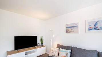 Un salon moderne doté d’un téléviseur à écran plat, d’un meuble TV en bois, d’un canapé gris et de deux tableaux accrochés au mur.
