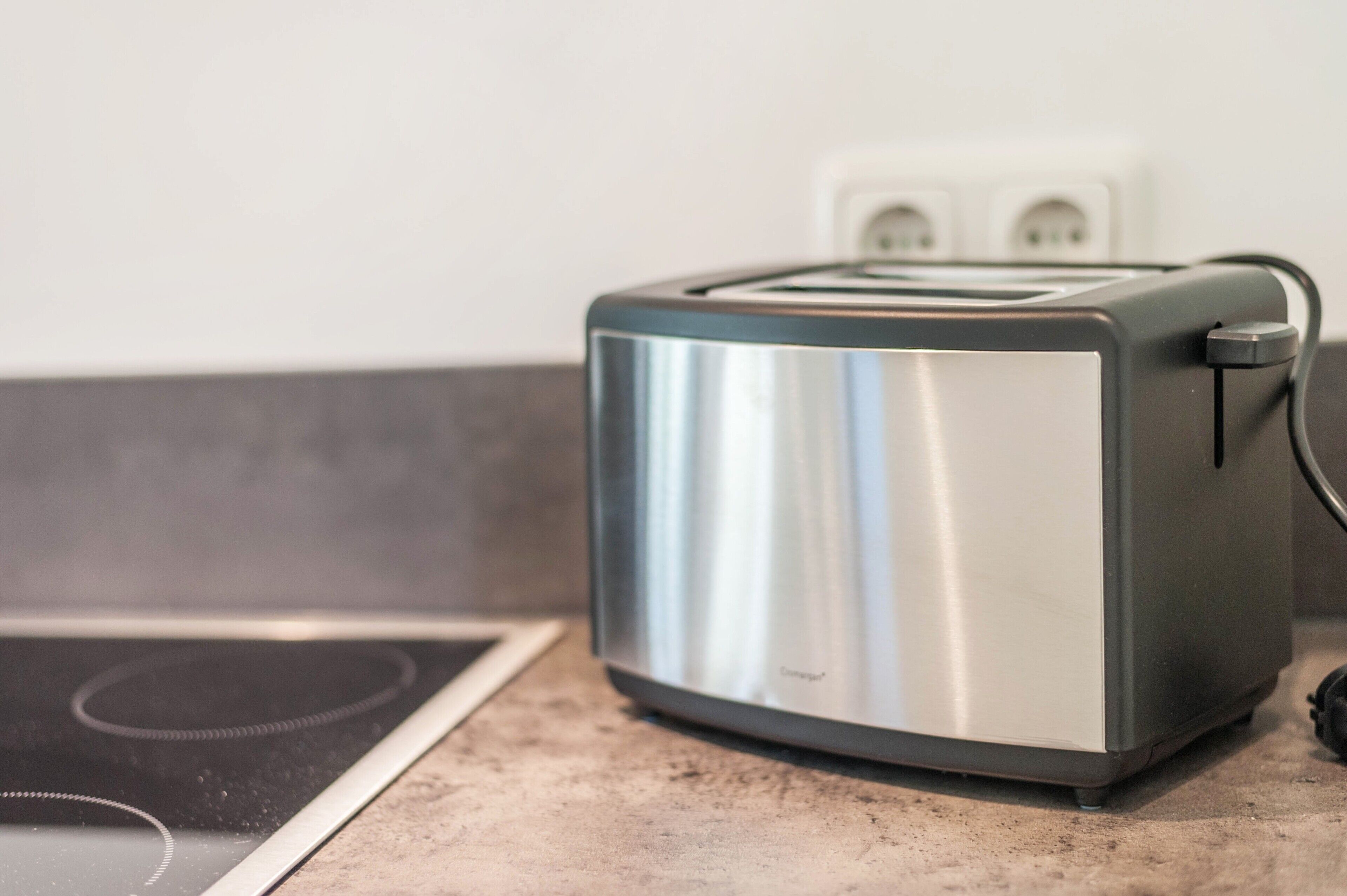 Eine moderne Küche mit einem Edelstahltoaster auf einer Arbeitsplatte, einem eingebauten Induktionskochfeld und einer Steckdose im Hintergrund.
