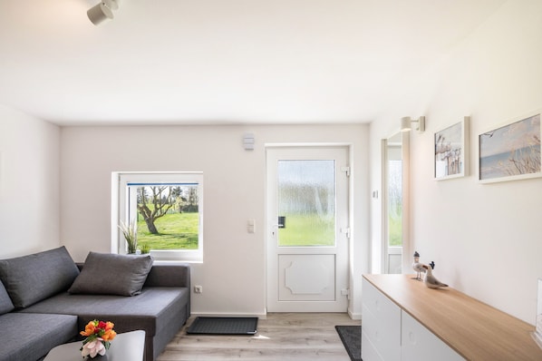 A modern living room with a grey sofa, a wooden side table, and a door leading to a balcony.