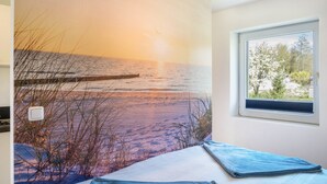 Una camera da letto con un grande murale raffigurante una spiaggia, una finestra vista alberi e un letto con coperta blu.
