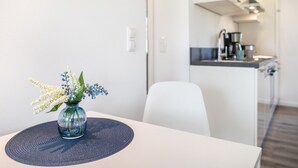 Una cucina moderna con una macchina da caffè, una zona pranzo bianca con un tavolo e un vaso di fiori.