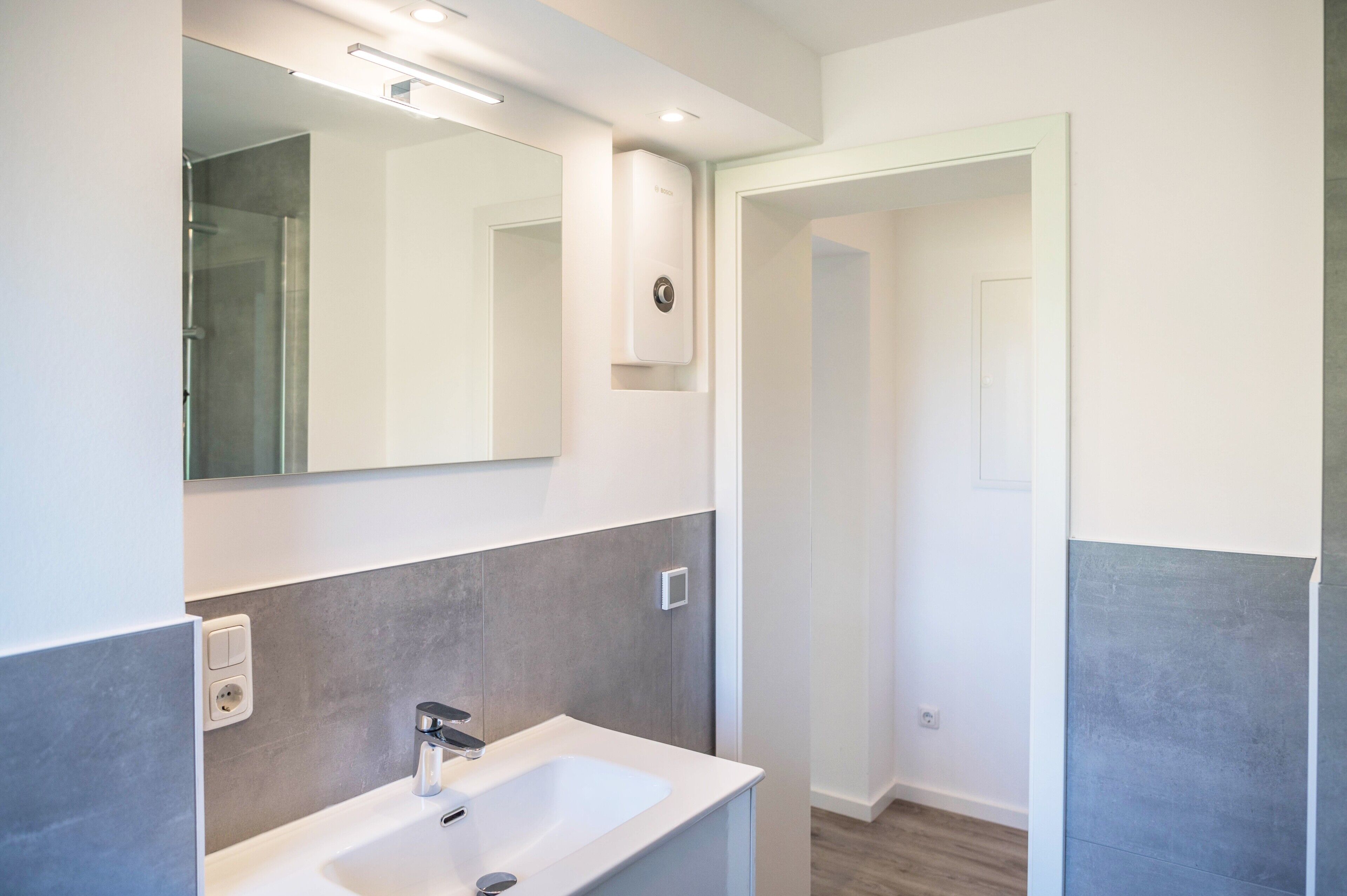 A modern bathroom with a white sink, a mirror, and a shower.