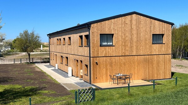 A wooden building with multiple windows and a patio area with outdoor seating.
