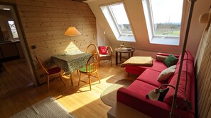 Un dormitorio tipo loft acogedor, con techo inclinado de madera, un sofá rojo, una mesa de comedor con sillas y un tragaluz.
