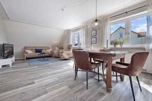 Una sala de estar moderna con comedor, suelo de madera, un conjunto de sofás y una mesa de comedor con sillas.