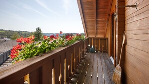 A wooden balcony with a view of the landscape, a broom leaning against the wall, and a window with a curtain. - Holiday Home 'Ferienhaus Sankt Peter' with Mountain View, Private Terrace and Wi-Fi (Dachsberg)