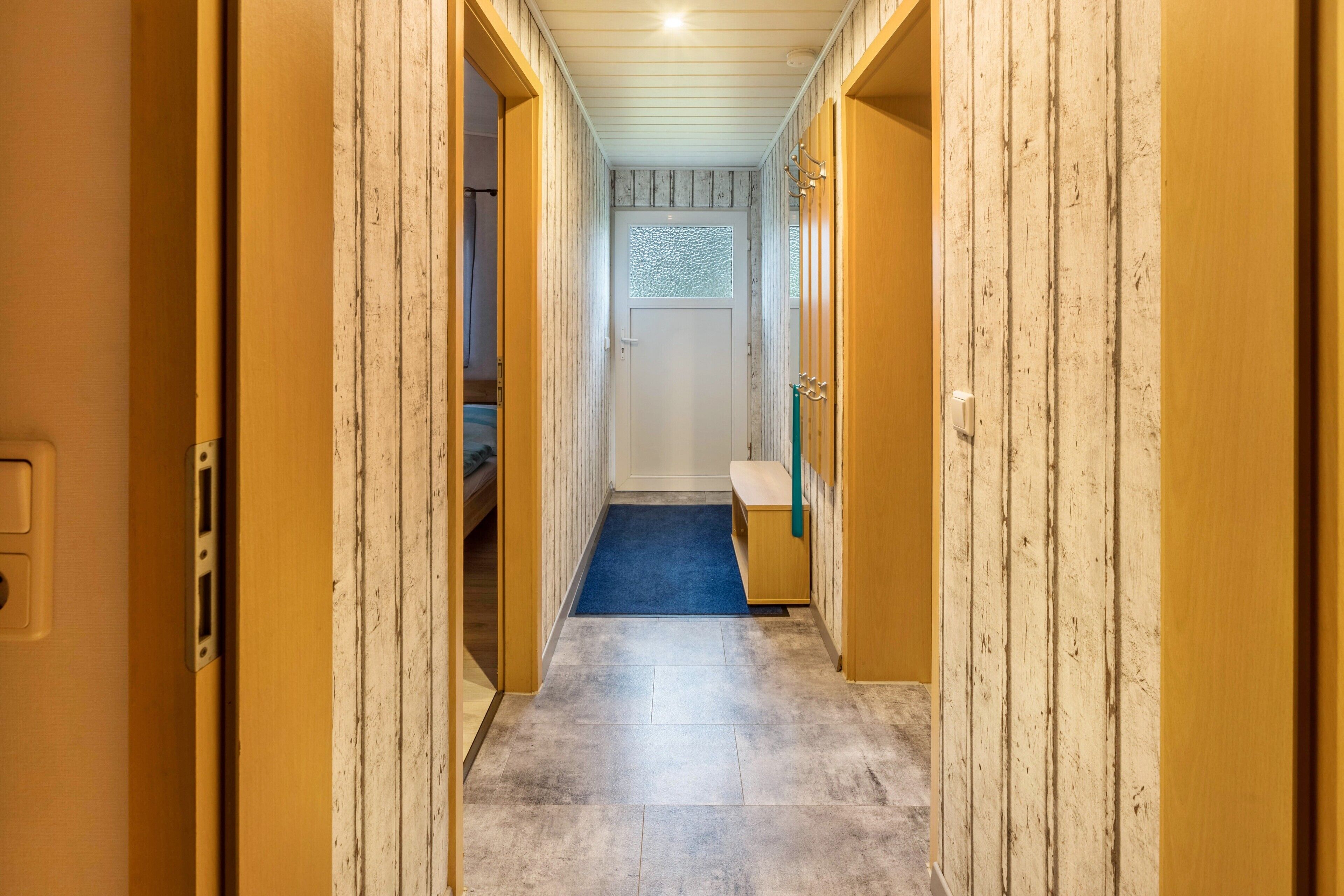 Un pasillo estrecho con paredes de madera y una alfombra azul que conduce a una puerta con ventanal esmerilado.