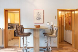 Una cocina moderna con armarios de madera, una mesa de comedor con dos taburetes altos y un dibujo enmarcado en la pared.
