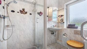 Ein Badezimmer mit Dusche, Toilette, Waschbecken und einem Fenster.
