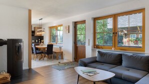 Una sala de estar moderna con un sofá, un comedor con sillas, un refrigerador y ventanas amplias con vistas a zonas verdes.