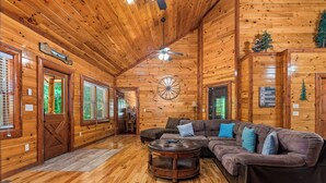 A wooden cabin interior with a large leather sofa, a wooden coffee table, and a ceiling fan.