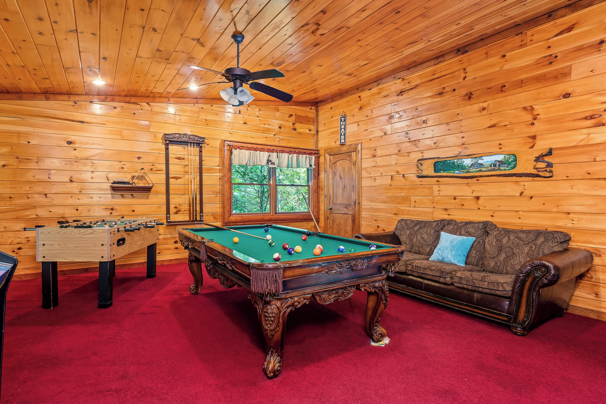 A wooden interior with a pool table, foosball table, and a sofa.