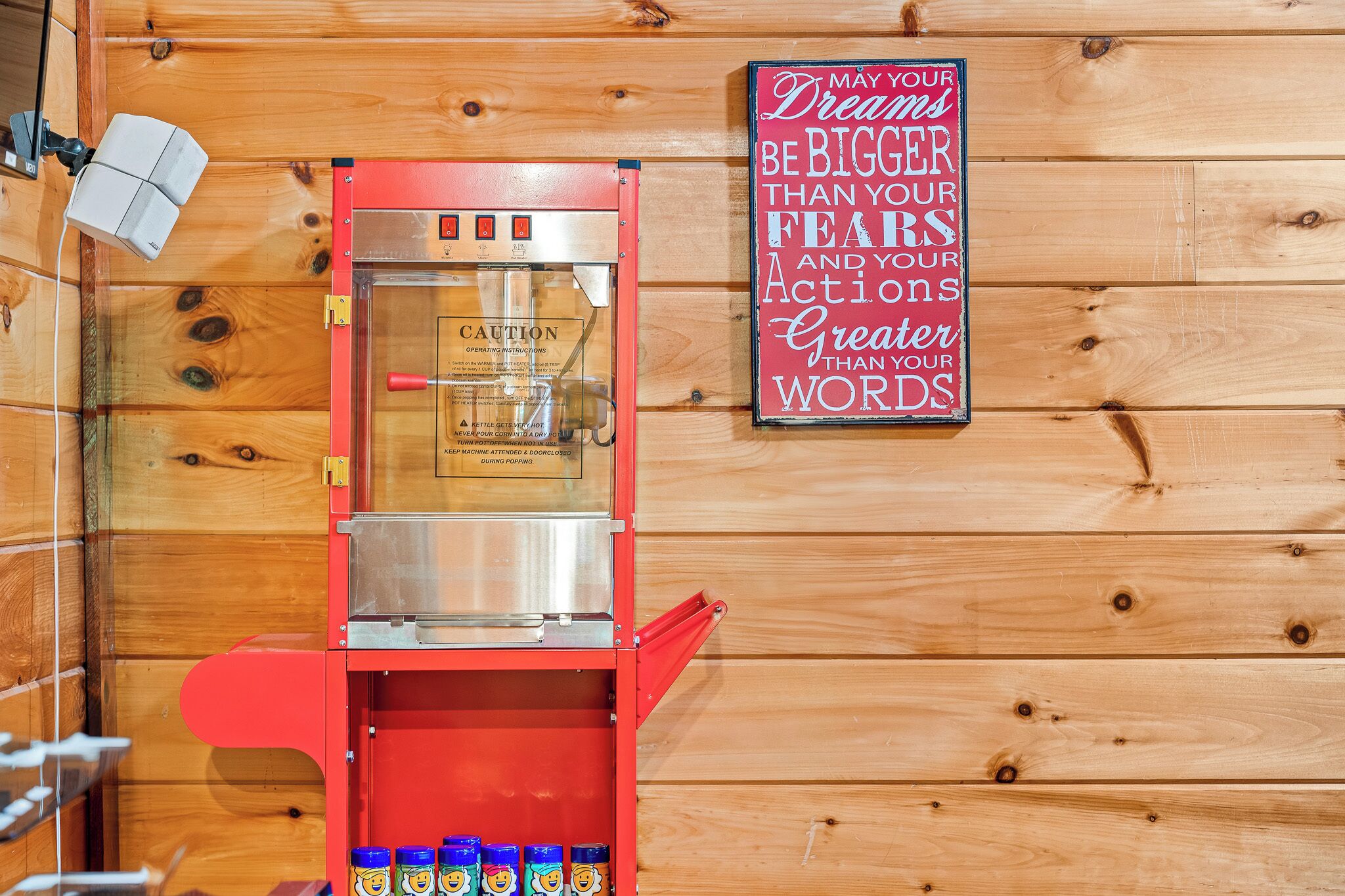 A coffee machine with a red exterior and a glass front, placed against a wooden wall with a motivational quote.