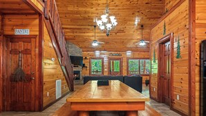 A wooden interior with a large wooden table, a chandelier, and a sign indicating the pantry.