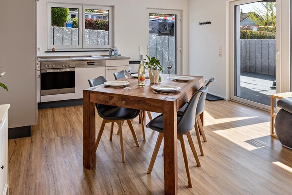 Uma cozinha moderna com uma mesa de jantar de madeira, cadeiras e vista para o quintal por uma porta de vidro deslizante.