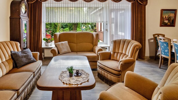 Ein Wohnzimmer mit einer Couch, Sesseln, einem Couchtisch, einer Uhr und einem Essbereich mit Tisch und Stühlen.