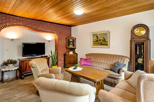 Ein Wohnzimmer mit Fernseher, Couch, Holz-Couchtisch und einer Uhr.