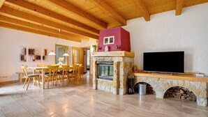Een eetruimte met een houten tafel en stoelen, een stenen openhaard met een televisie, en een houten plafond.