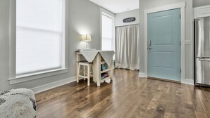 A room with a wooden floor, a light blue door, a white table with a lamp, and a laundry sign on the wall. - *Sleeps 4* Downtown USA ~ Walkable Dickson Apt (Dickson)