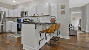 A modern kitchen with white cabinets, stainless steel appliances, and a bar area with two stools. - *Sleeps 4* Downtown USA ~ Walkable Dickson Apt (Dickson)