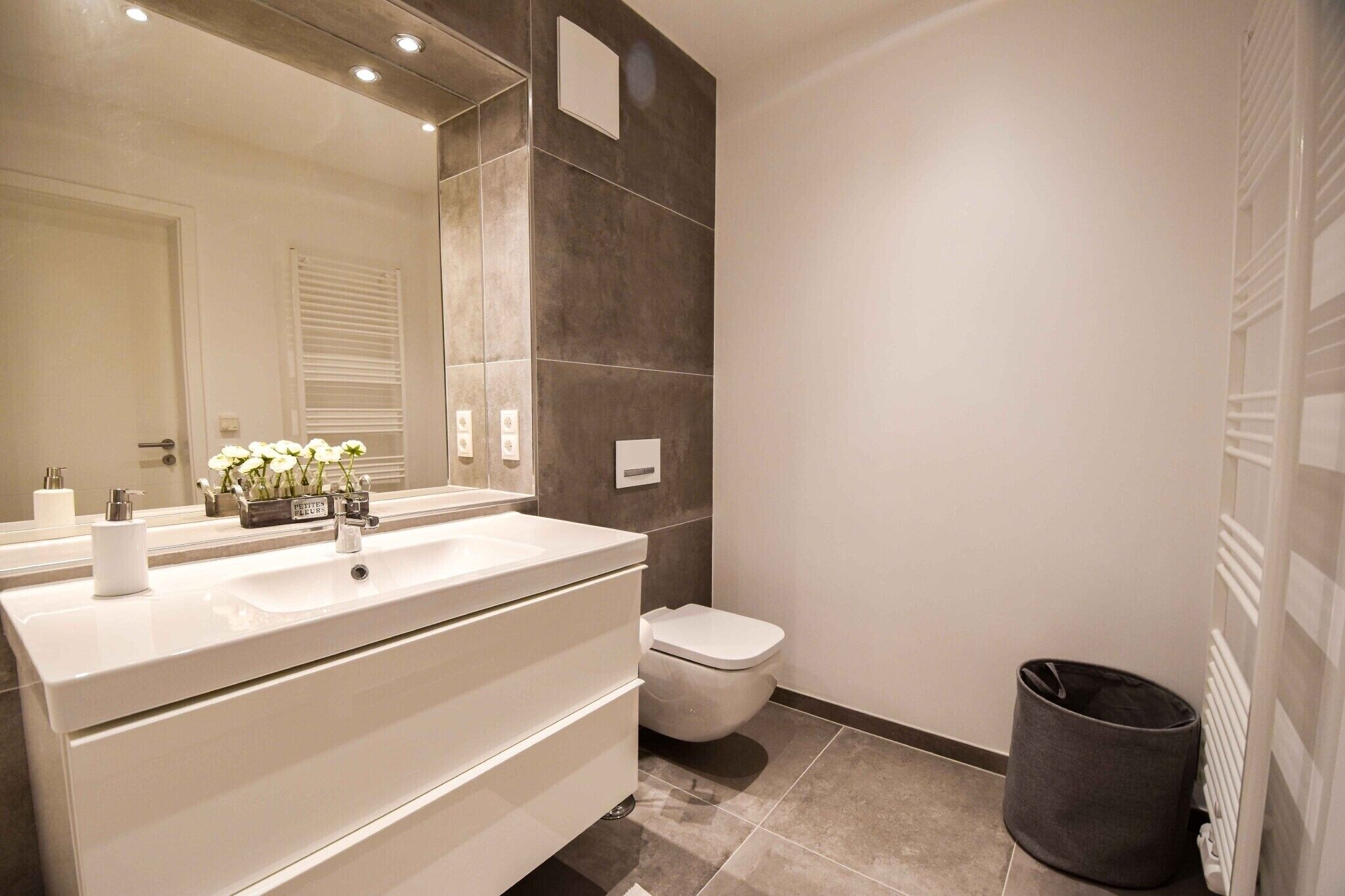 Une salle de bain avec un meuble-lavabo blanc, un miroir, des toilettes et une poubelle.