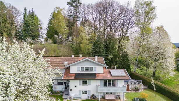 Een tweelaags huis met schuin dak, balkon en tuin.