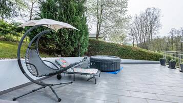 Um terraço no telhado com espreguiçadeira, guarda-sol e banheira de hidromassagem.