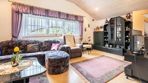 Een woonkamer met een bank, fauteuil, poef, salontafel en een boekenkast.