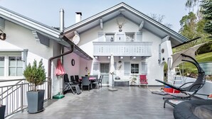Een ruim terras met een eethoek, tuinmeubilair en een wit gebouw met balkon.