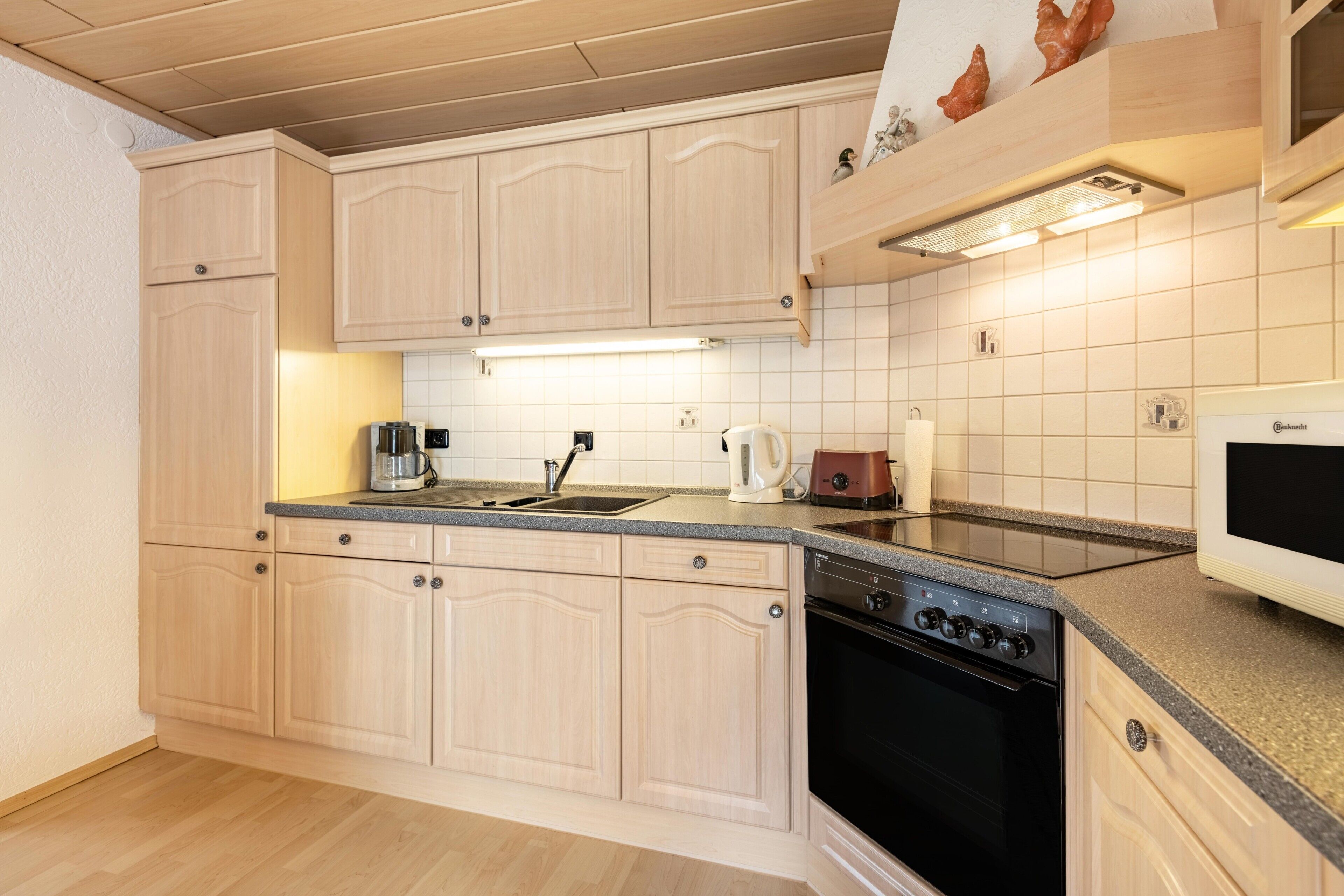 A modern kitchen with light wood cabinets, a black oven, a microwave, and a coffee maker.