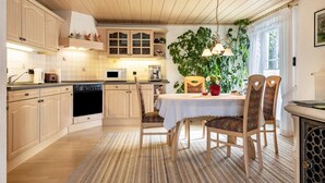 Een keuken met houten kastjes, een eettafel met stoelen en een grote potplant.
