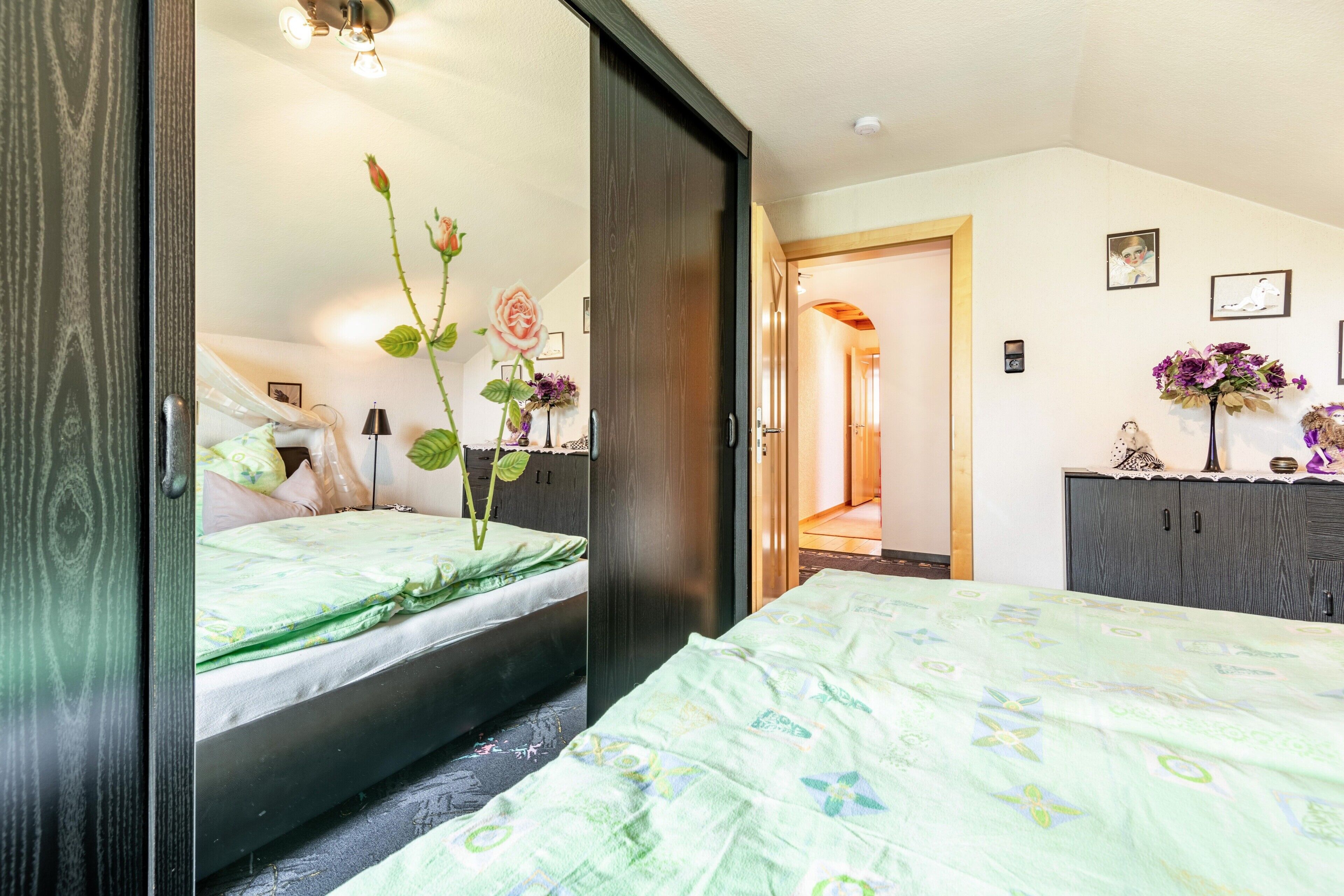 Une chambre à coucher comprenant un lit, une commode, un miroir et une porte donnant sur une autre pièce.