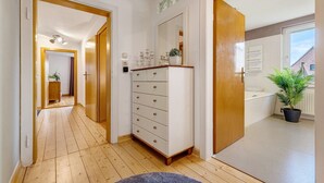 A hallway with wooden flooring, a white dresser with drawers, a mirror, and a potted plant. - Apartment 'Weserberglandblumen' with Mountain View, Private Garden and Wi-Fi (Bad Pyrmont)