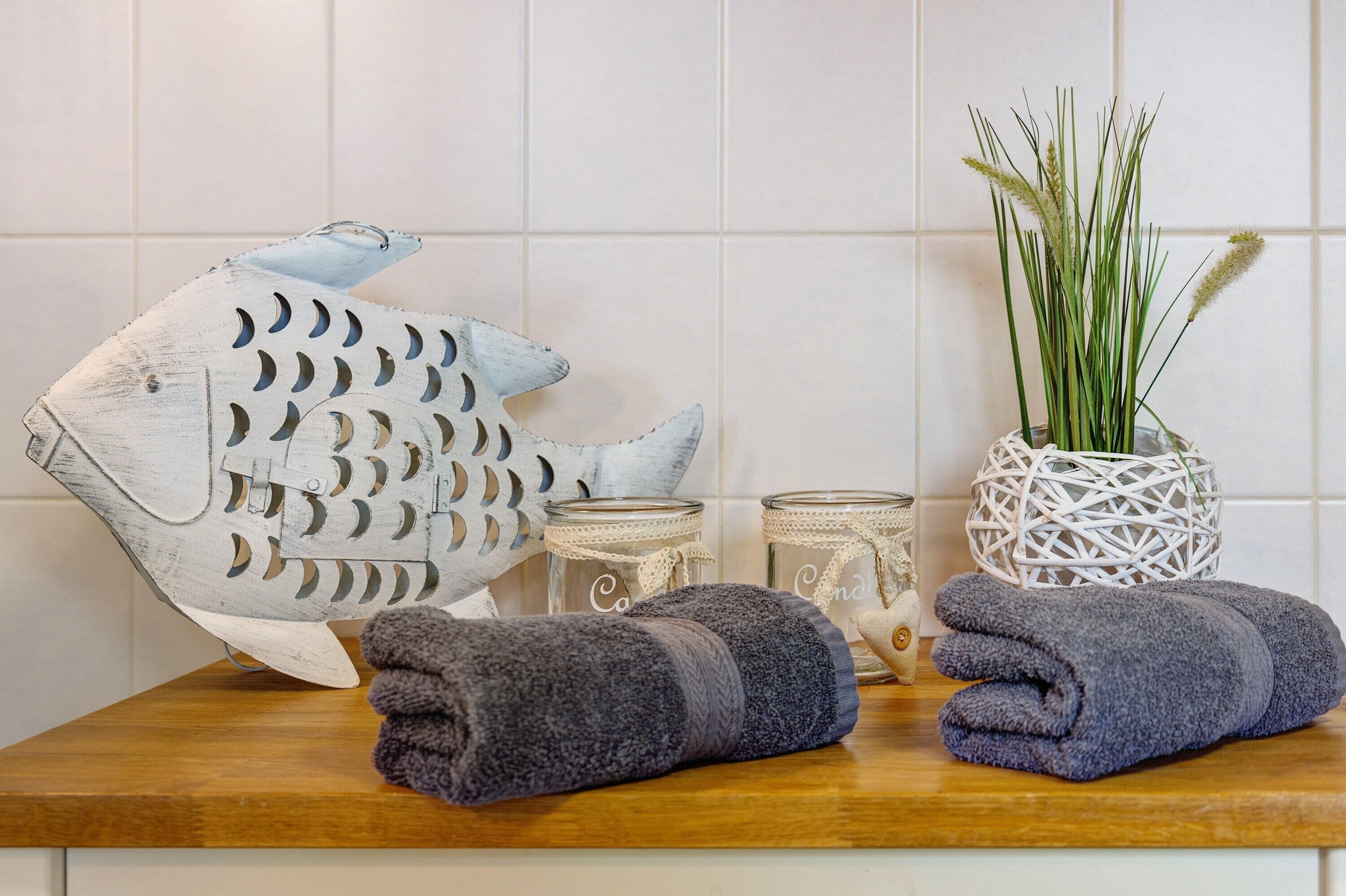 A wooden table with a decorative fish sculpture, a woven basket with green plants, candles, and folded towels.