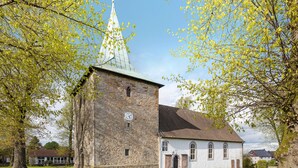 A stone church with a clock tower, a white building with arched windows, and a pathway leading to the church. - Apartment 'Weserberglandblumen' with Mountain View, Private Garden and Wi-Fi (Bad Pyrmont)