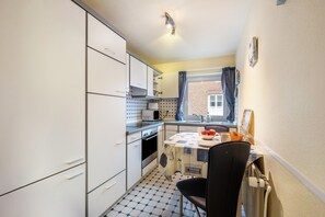 Une cuisine compacte avec des meubles blancs, un four à micro-ondes, une cuisinière et une table à manger avec une chaise.