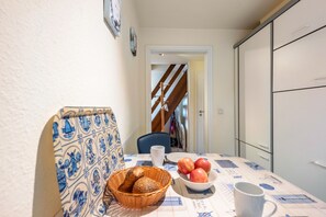 Une table à manger avec un panier de pain, un saladier de pommes et une tasse.