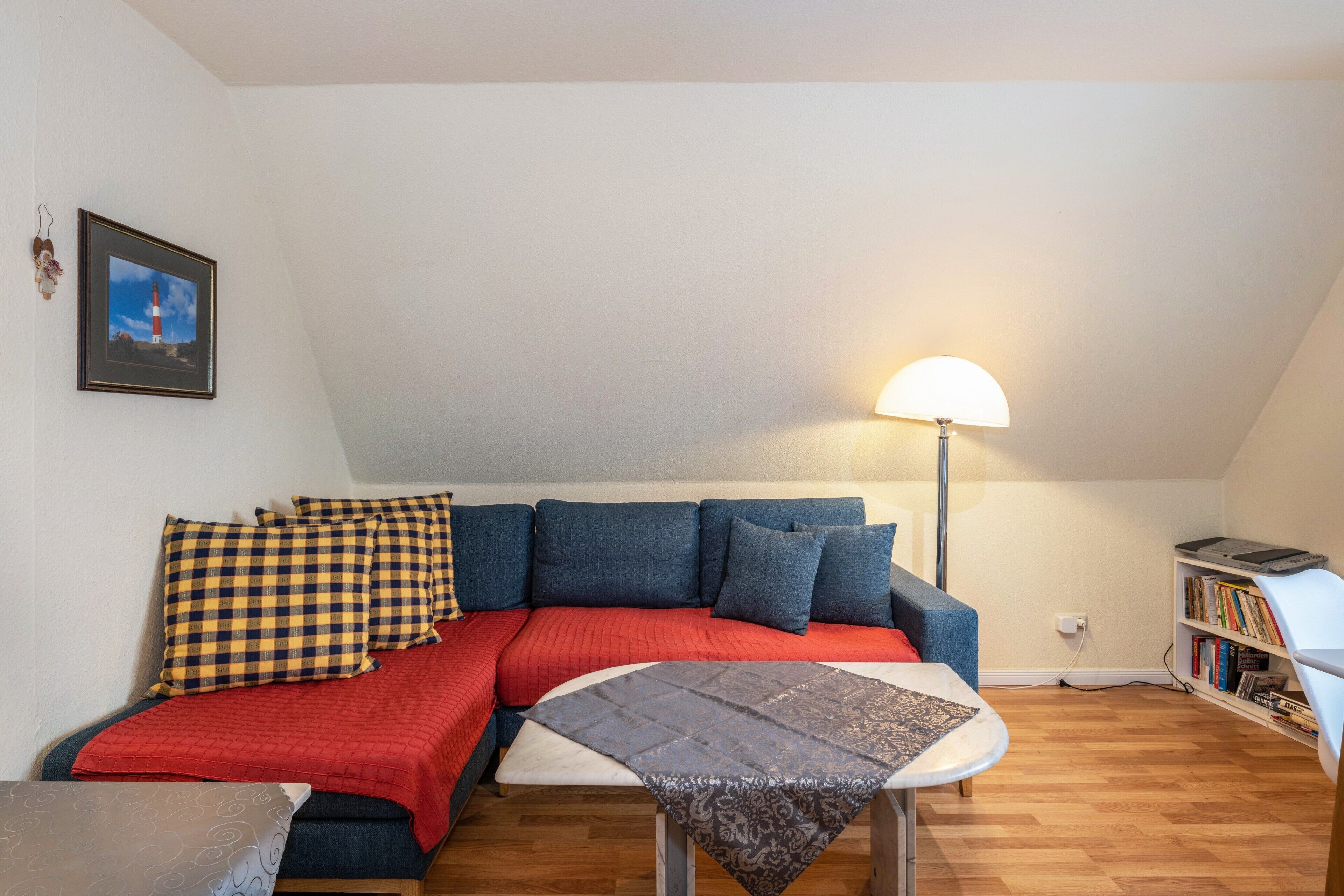 Een gezellige woonkamer met een bank, een tafeltje, een lamp en een boekenkast.