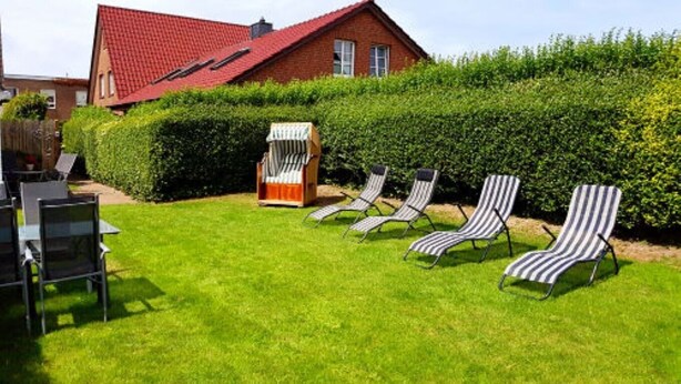 Um quintal com uma casa de telhado vermelho, um hedge e quatro cadeiras de lounge listradas.
