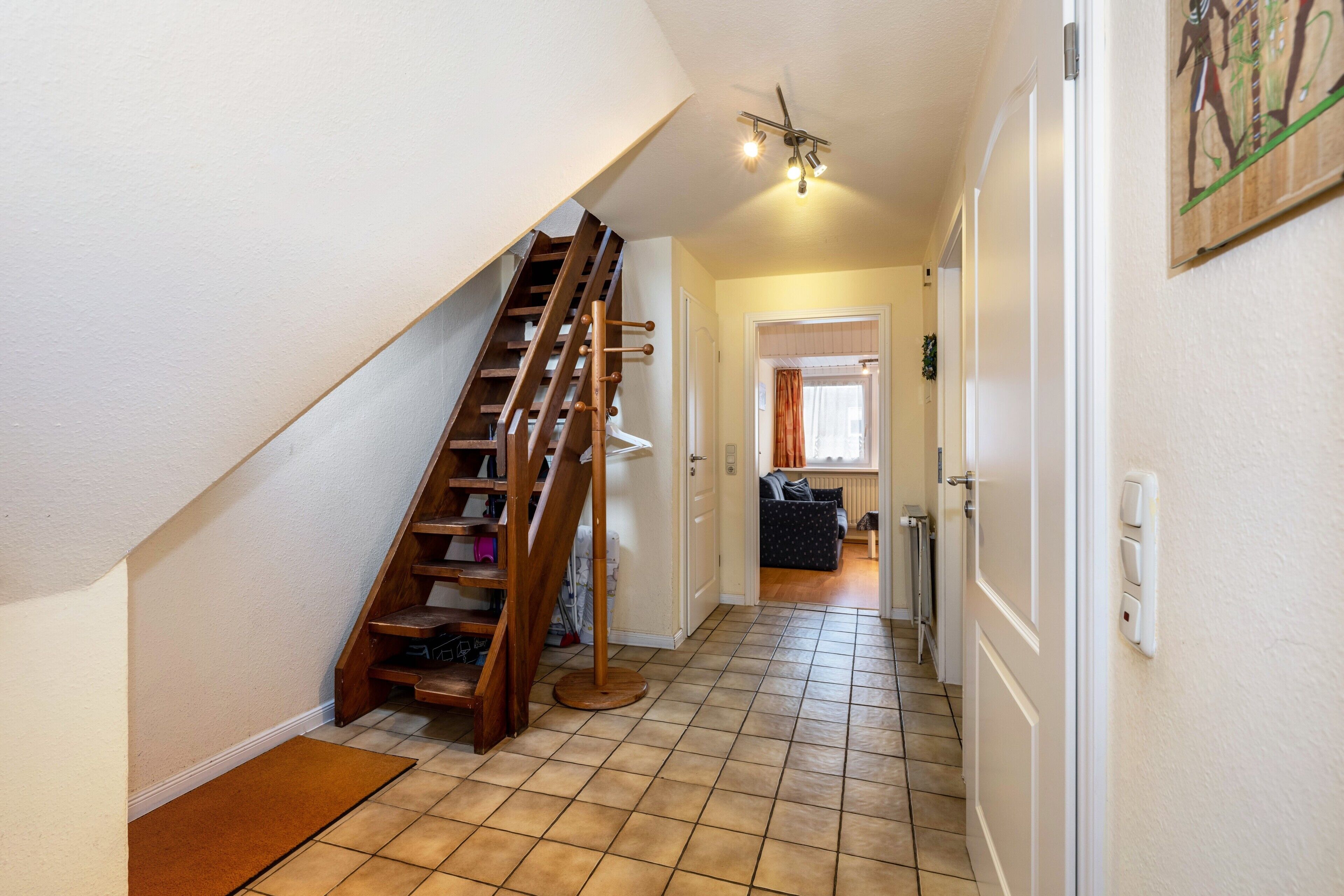 A staircase leading to a landing, a hallway with a tiled floor, and a door leading to another room.