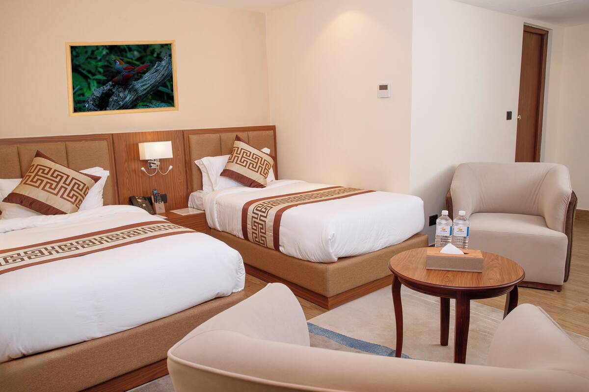 Una habitación de hotel con dos camas, una zona de estar con una mesa y una puerta.